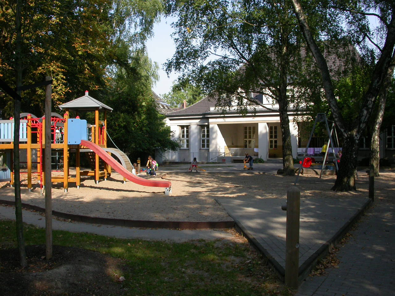 Klettergerüst im Außenspielbereich und Blick auf die Rückfront des Tageseinrichtung für Kindergebäudes.