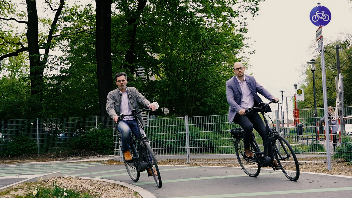 Norbert Hudde (l.) und Marcus Beyer auf dem Fahrrad im Bereich der Schmiedestraße auf der neuen Promenade. Screenshot: Stadt Krefeld, Presse und Kommunikation, Ramona Bietenbeck